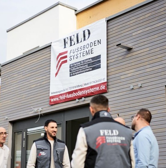Mitarbeiter von Feld Fußbodensysteme stehen in Arbeitskleidung vor einem Gebäude.