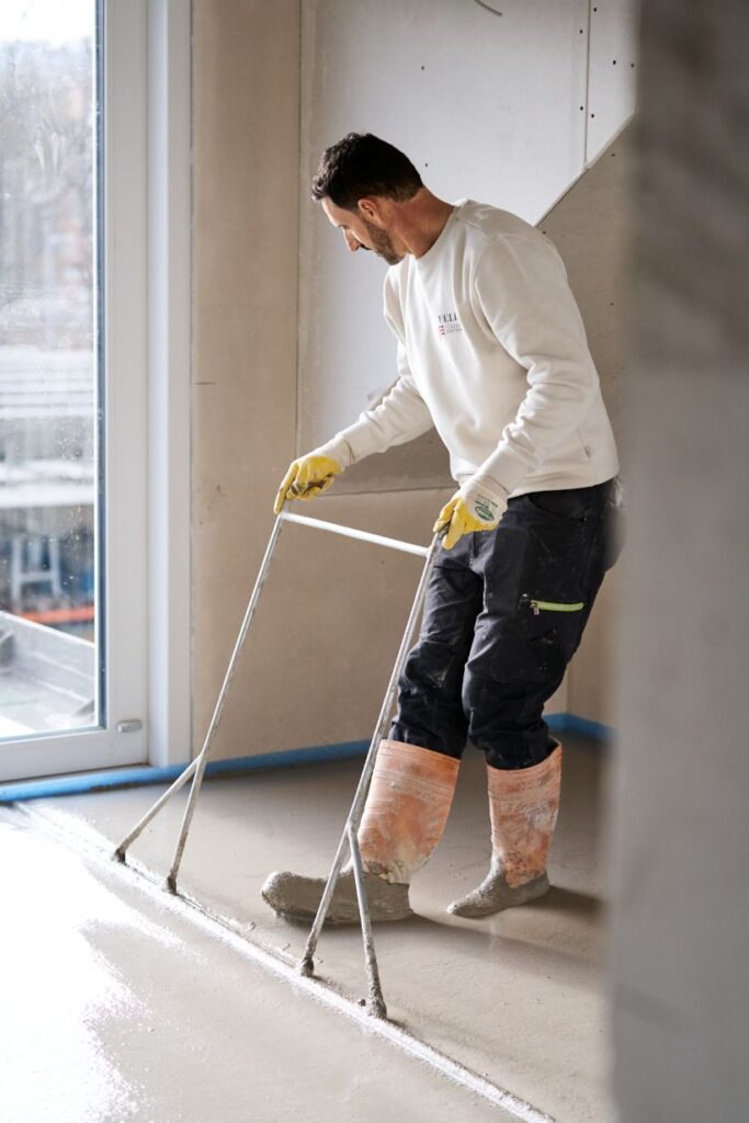 Ein Mitarbeiter von Feld Fußbodensysteme bringt Estrich fachgerecht ein.